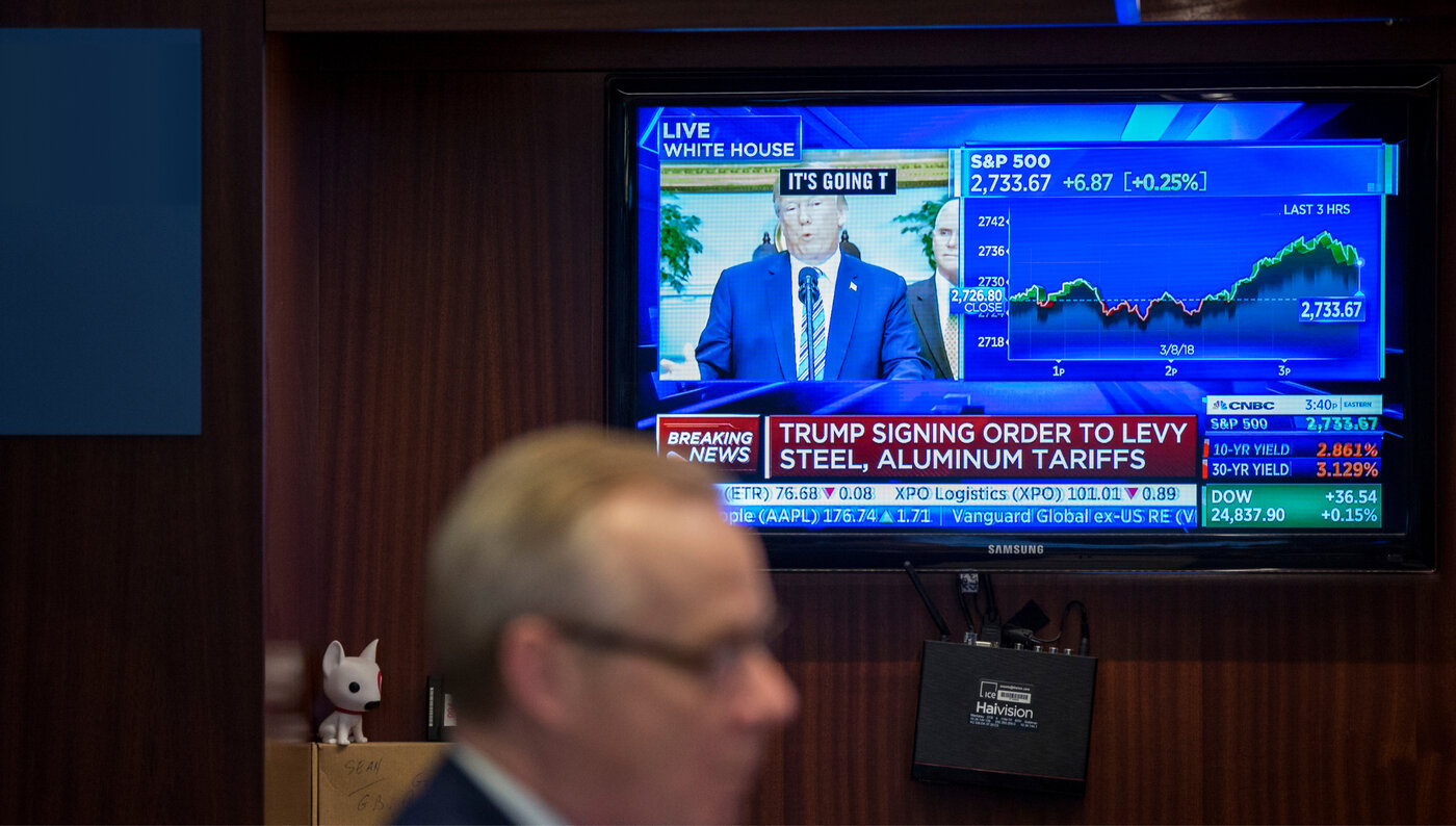 A stockbroker works as a TV in the background reports on Trump's steel and aluminum tariffs