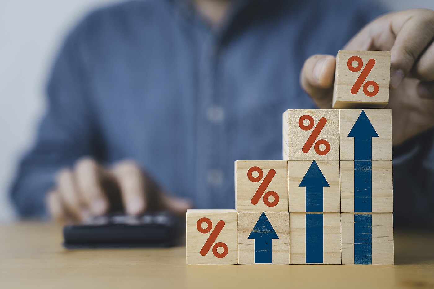 A man with a calculator stacking cubes with red percentage signs and blue arrows.